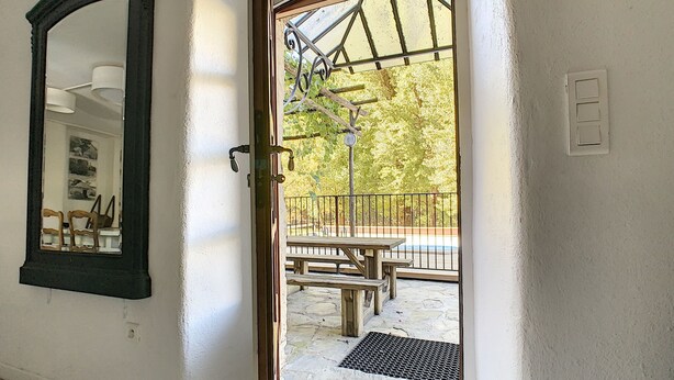 Une porte-fenêtre donnant sur un patio extérieur, avec une table et des chaises en bois, une rambarde en métal et une vue sur les arbres.