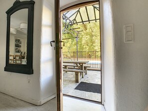 Een doorgang naar een terras buiten, met een houten tafel en stoelen, een metalen hekwerk en uitzicht op bomen.