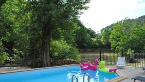 Une piscine avec une terrasse en bois, entourée d’arbres et d’une clôture.