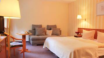 A hotel room with a bed, a sofa, a small table with a lamp, and a television.