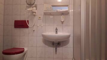A bathroom with a toilet, sink, mirror, and a red bucket.