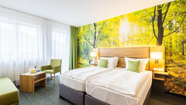 Ein Hotelzimmer mit zwei Betten, einem Schreibtisch, einem Stuhl und einer großen Wandmalerei von einem Wald.