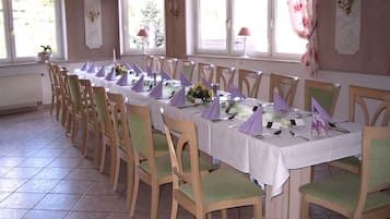Una larga mesa de comedor con sillas, un valance floral en la ventana y una araña.