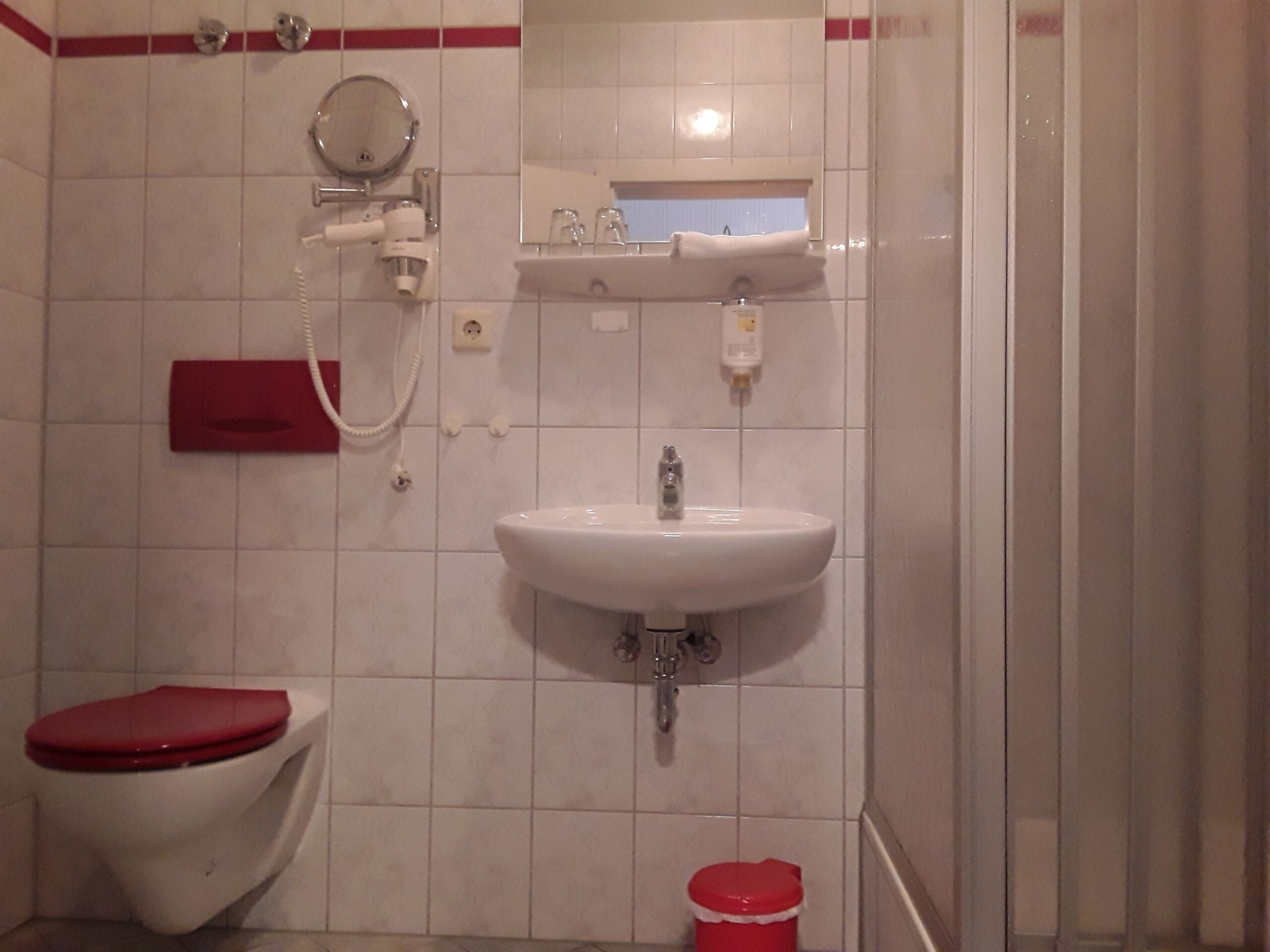 Une salle de bain équipée d’un WC, d’un lavabo, d’un miroir et d’un seau rouge.