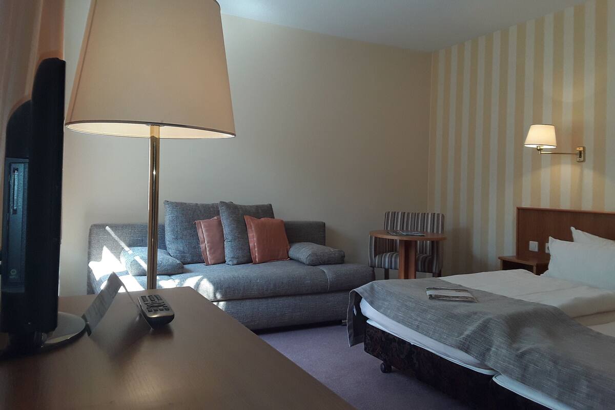 Una habitación de hotel con una cama, un sofá, un escritorio con lámpara, un televisor y una mesita.