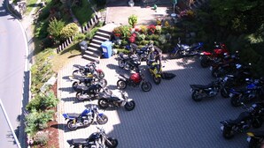 Ein Parkplatz mit mehreren Motorrädern und Rollern, umgeben von Grünflächen und Stufen, die zu einem Gebäude führen.