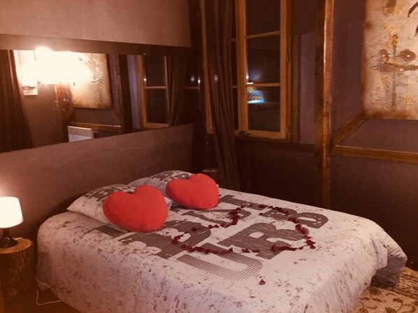 Una cama con una colcha estampada y dos almohadas rojas con forma de corazón.