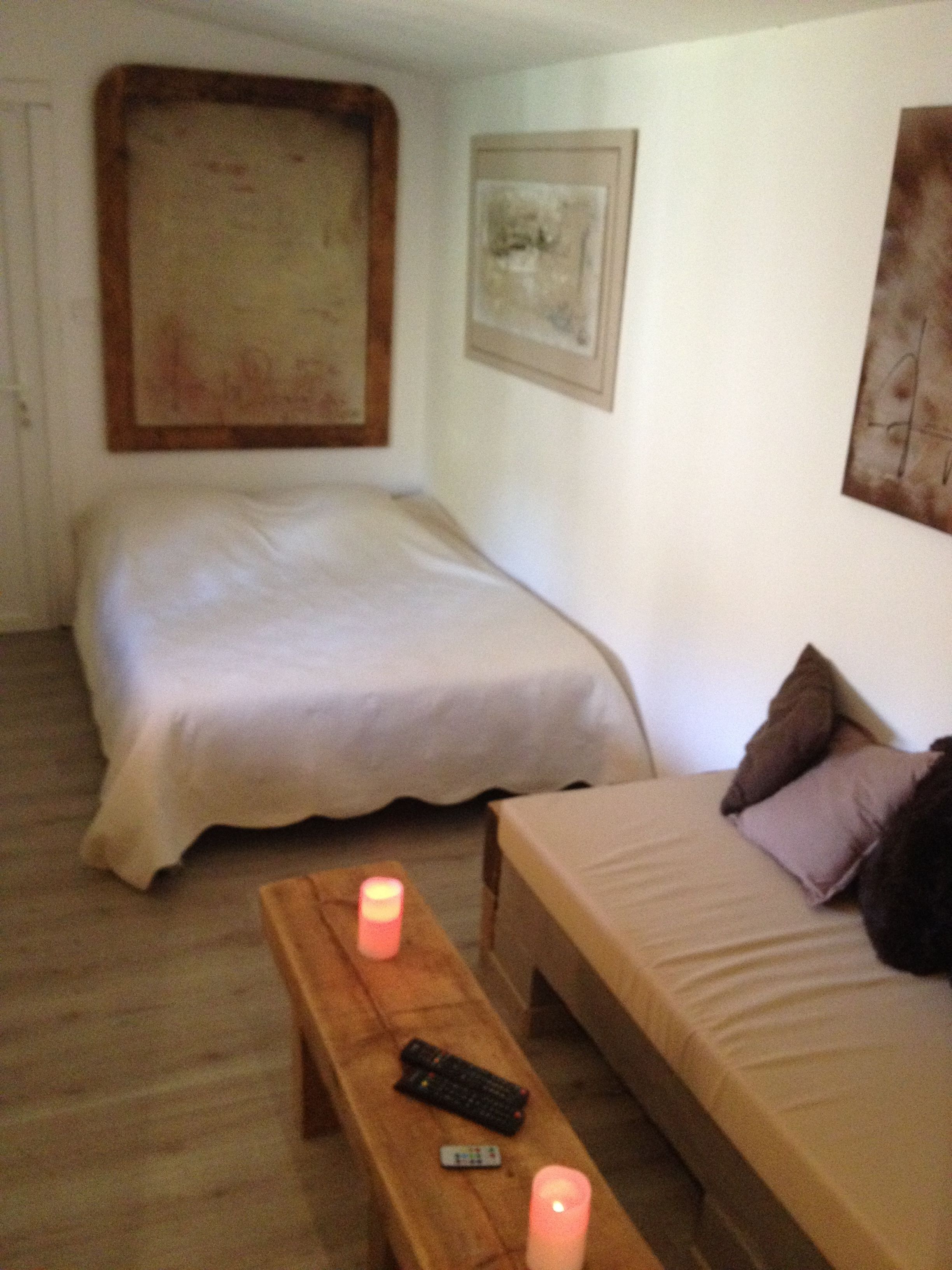 A bedroom with two beds, a wooden bench, and two lit candles.