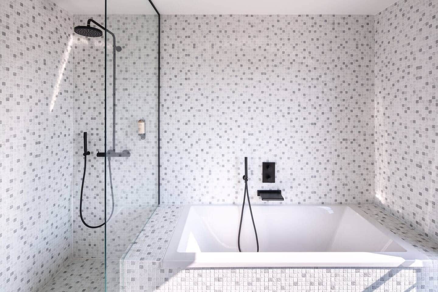 A modern bathroom with a freestanding bathtub, a glass-enclosed shower area, and a tiled wall with a geometric pattern.