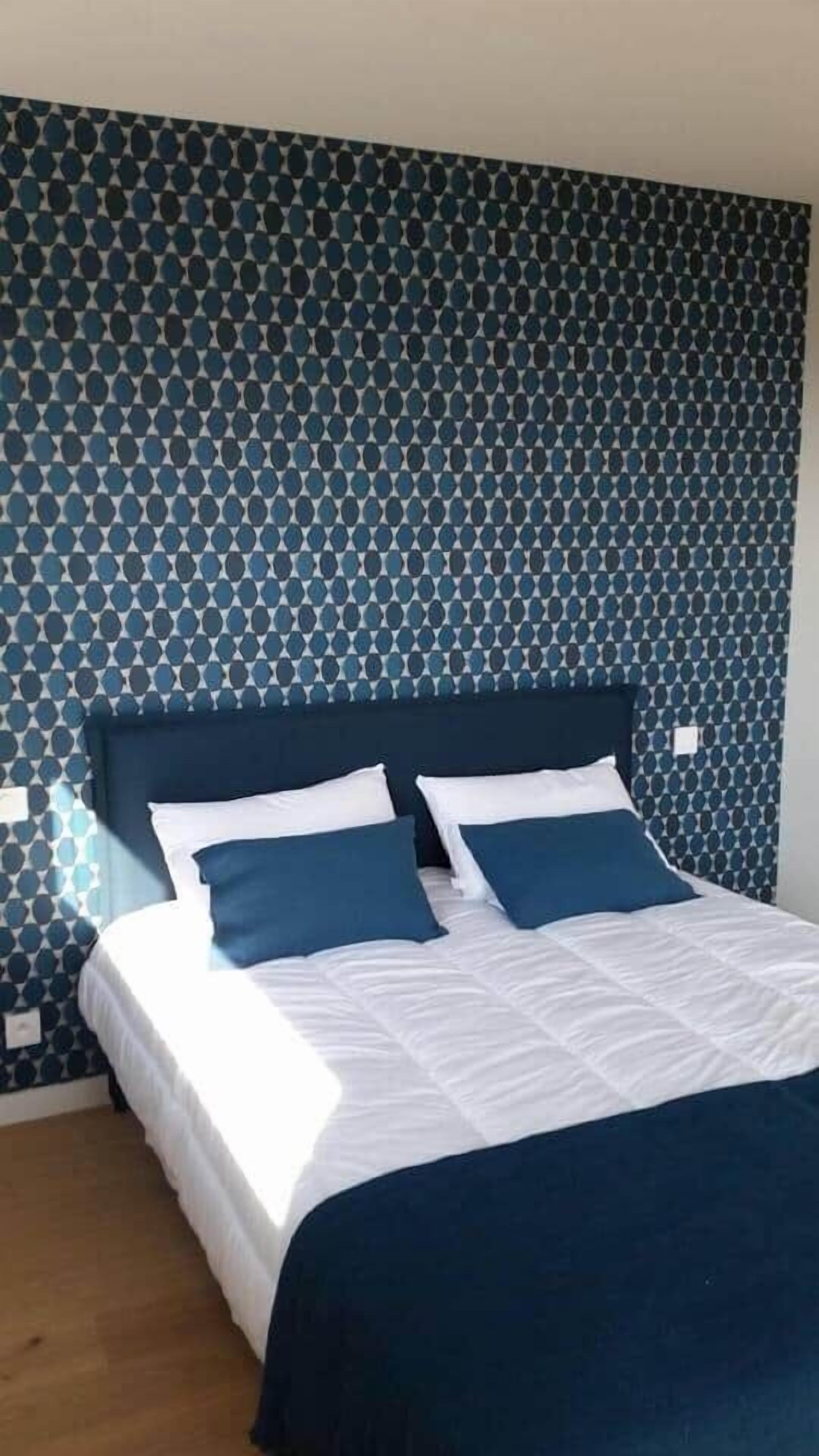 A bed with a dark headboard, white bedding, and two blue pillows.