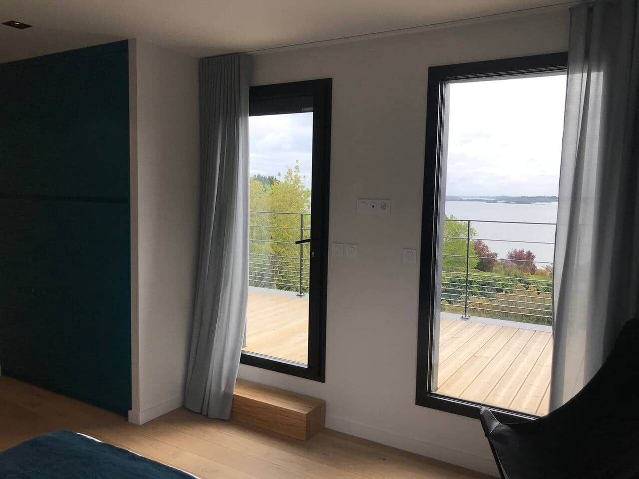 Ein modernes Zimmer mit großem Fenster, Holzboden und Blick auf einen mit Grünpflanzen bepflanzten Balkon.