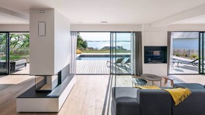 A modern living room with a large sofa, a TV, and a view of a wooden deck and ocean. - To complete (Saint-Cast-le-Guildo)