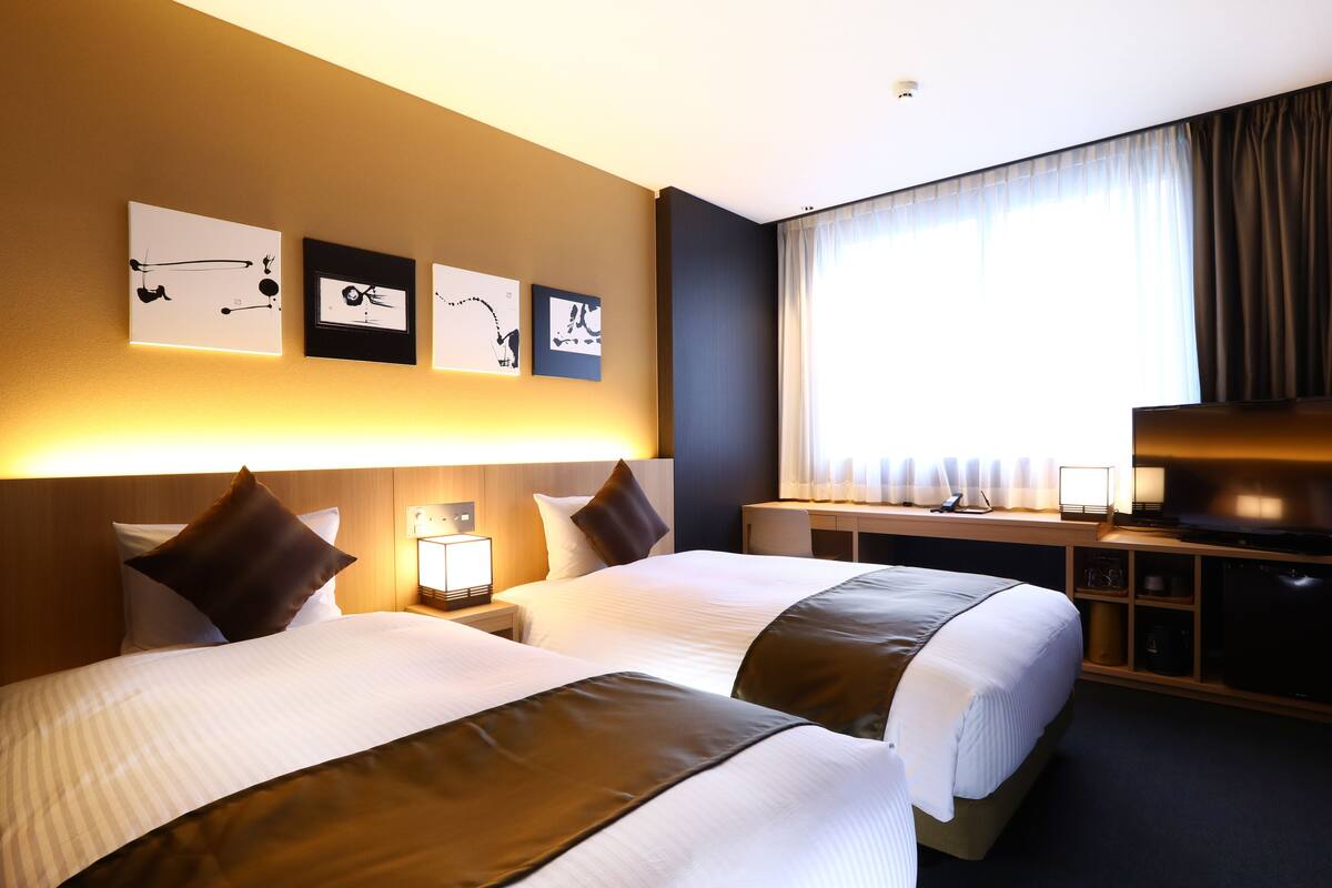 Ein Hotelzimmer mit zwei Betten, einem Schreibtisch, einem Fernseher und Bildern an der Wand.