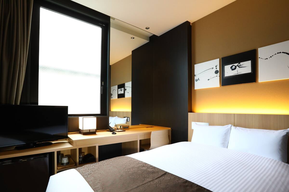 Ein Hotelzimmer mit einem großen Bett, einem Schreibtisch mit Computer, einem Fernseher und einem Fenster mit Vorhängen.