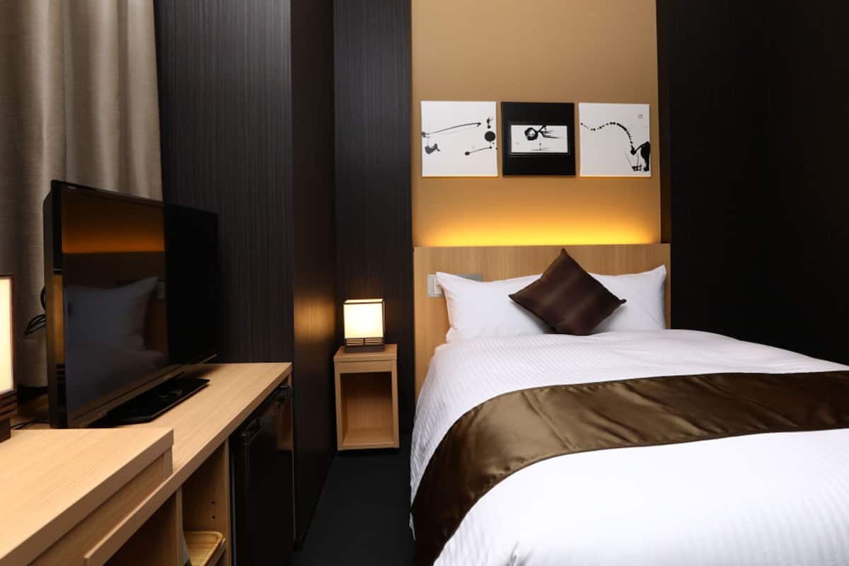 Ein Hotelzimmer mit einem Bett, einem Fernseher, einem Schreibtisch und einem Nachttisch.