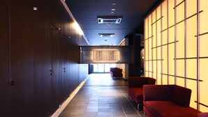 Un pasillo moderno con puertas de madera oscura, asientos rojos y una gran pared iluminada.