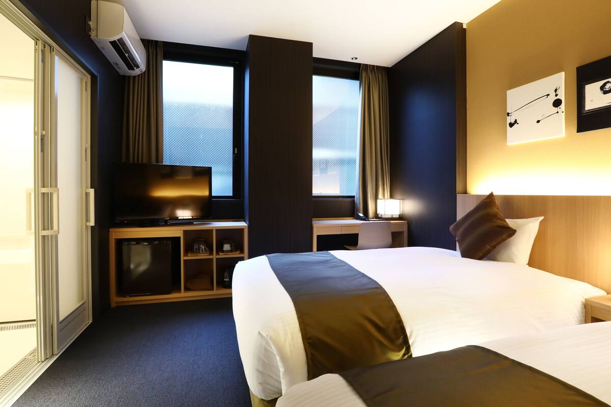 Ein Hotelzimmer mit einem großen Bett, einem Schreibtisch mit Fernseher, einer Minibar und einem Vorhangfenster.