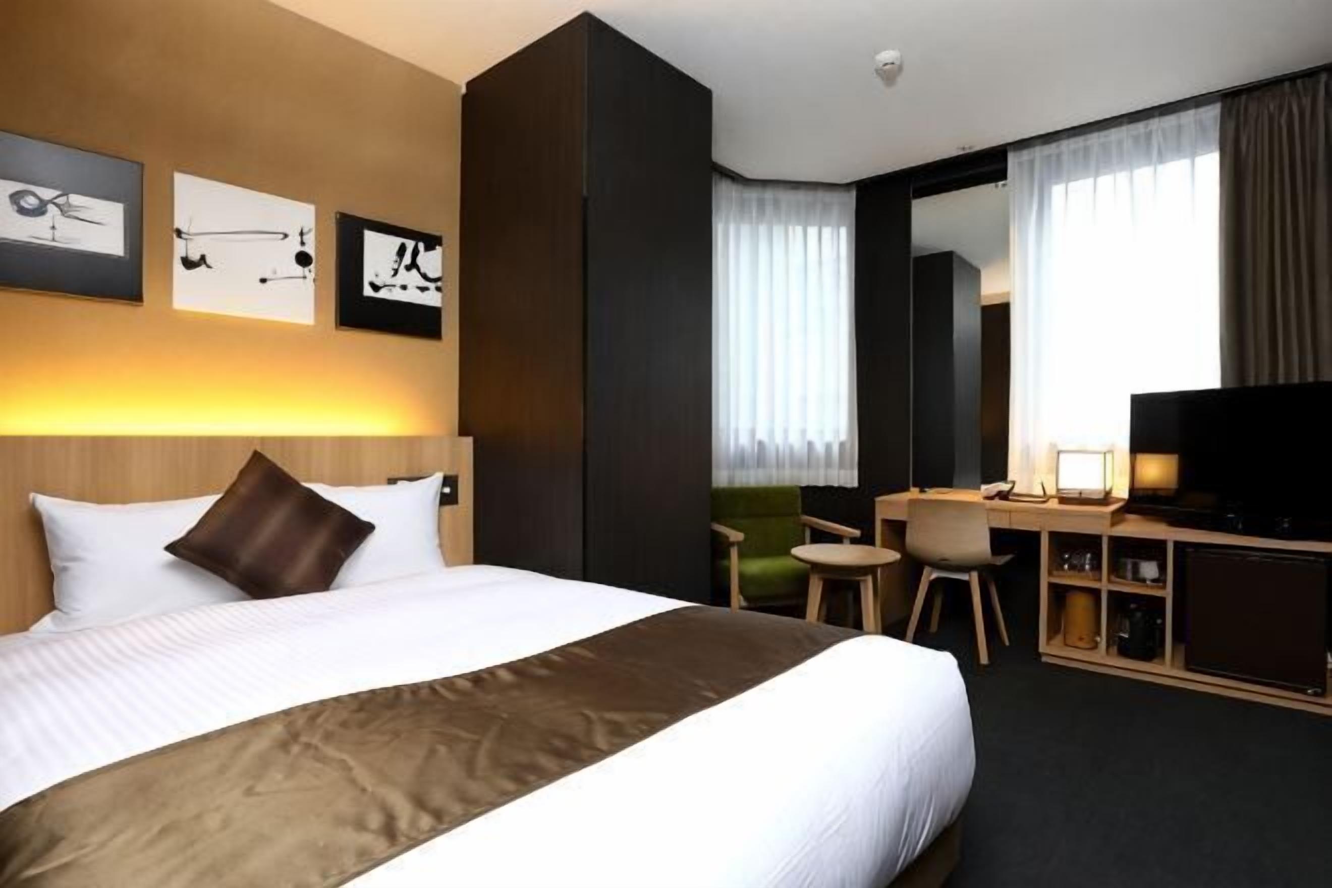 Quarto de hotel com uma cama grande, uma escrivaninha com cadeira, televisão e obras de arte na parede.