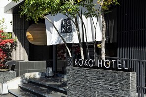 Ein Hotel Eingang mit einem Schild, auf dem 'KOKO HOTEL' steht, und eine Steinsäule mit Stufen, die zum Eingang führen.