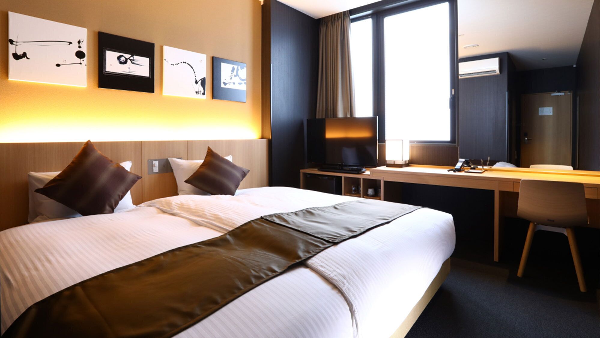 Ett hotellrum med en stor säng, ett skrivbord, en tv och konstverk på väggen.