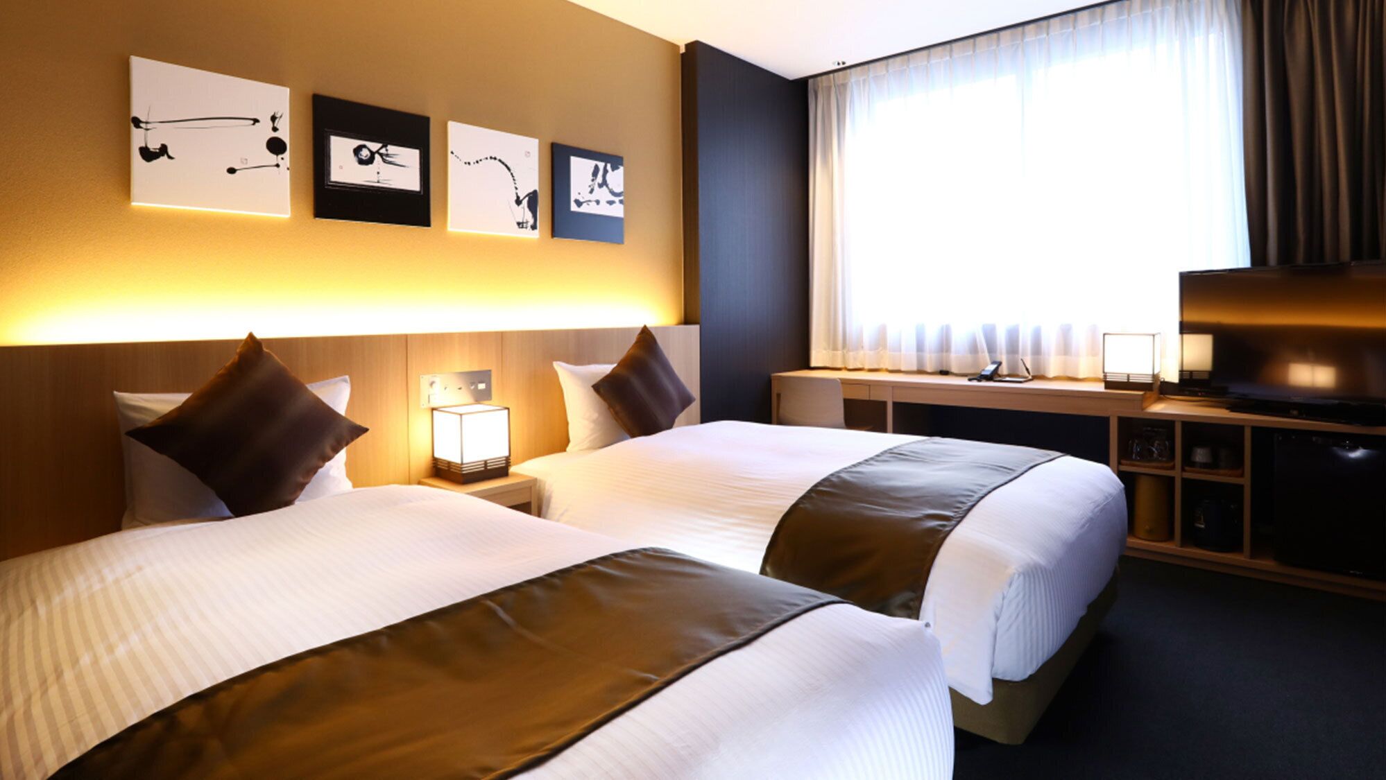 Ett hotellrum med två sängar, ett skrivbord med en tv, en lampa och konstverk på väggen.