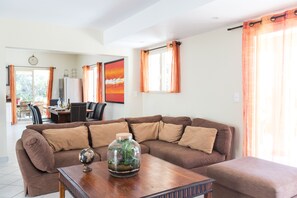 A living room with a brown sectional sofa, a wooden coffee table with a globe and a glass terrarium, and a dining area in the background.