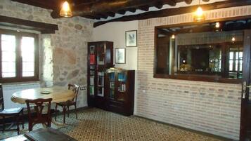 A room with a stone wall, wooden ceiling, a round table with chairs, a wooden cabinet with glass doors, and a patterned floor.