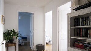 A room with a wooden floor, a bookshelf filled with books, a potted plant, and a bed with a blue and white patterned bedspread. - Large house, on land of 1000m2, 150m from the beach, 4 bedrooms, WIFI (Concarneau)