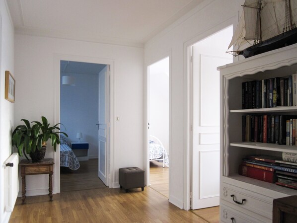A room with a wooden floor, a bookshelf filled with books, a potted plant, and a bed with a blue and white patterned bedspread.
