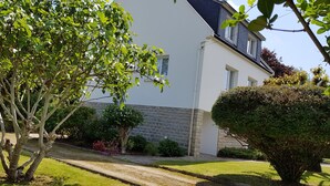 A house with a stone wall, a lawn, and a tree in the foreground. - Large house, on land of 1000m2, 150m from the beach, 4 bedrooms, WIFI (Concarneau)