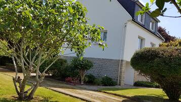 Une maison avec un mur en pierre, une pelouse et un arbre au premier plan.