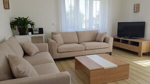 A modern living room with beige sofas, a wooden coffee table, a TV on a wooden stand, and a potted plant. - Large house, on land of 1000m2, 150m from the beach, 4 bedrooms, WIFI (Concarneau)