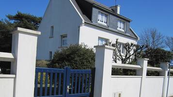 Une maison à deux étages, avec une façade blanche, un portail bleu et une pancarte indiquant qu’il s’agit d’une propriété privée.