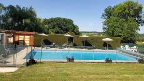 Piscina com espreguiçadeiras e guarda-sóis, rodeada por um jardim bem cuidado e árvores.