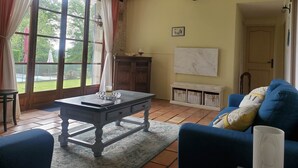 Quarto com uma janela grande, uma mesa com um vaso, um sofá azul e um armário com cestos.