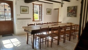 Uma área de refeições com uma mesa e cadeiras de madeira, uma janela com vista para o exterior e um quadro na parede.