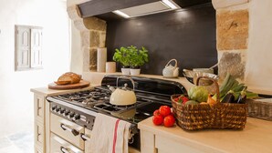 A kitchen with a gas stove, oven, and a large black range hood. There are potted plants and a basket of vegetables on the counter. - Luxury Cottage, Outdoor Nordic Hot Tub and Sauna, D-Day Beaches 15 km (Isigny-Sur-Mer)