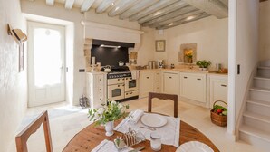 A kitchen with a stove, oven, and a dining area with a table set for two. - Luxury Cottage, Outdoor Nordic Hot Tub and Sauna, D-Day Beaches 15 km (Isigny-Sur-Mer)