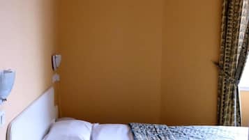 Una cama individual con ropa de cama blanca, una mesita de noche con un control remoto y una colcha estampada.