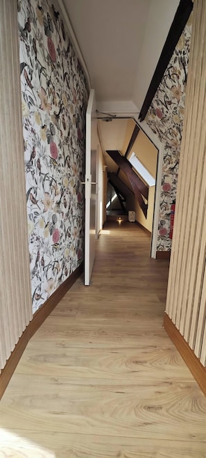 Ein Flur mit Holzboden, floralem Wandpapier und einer schrägen Decke.