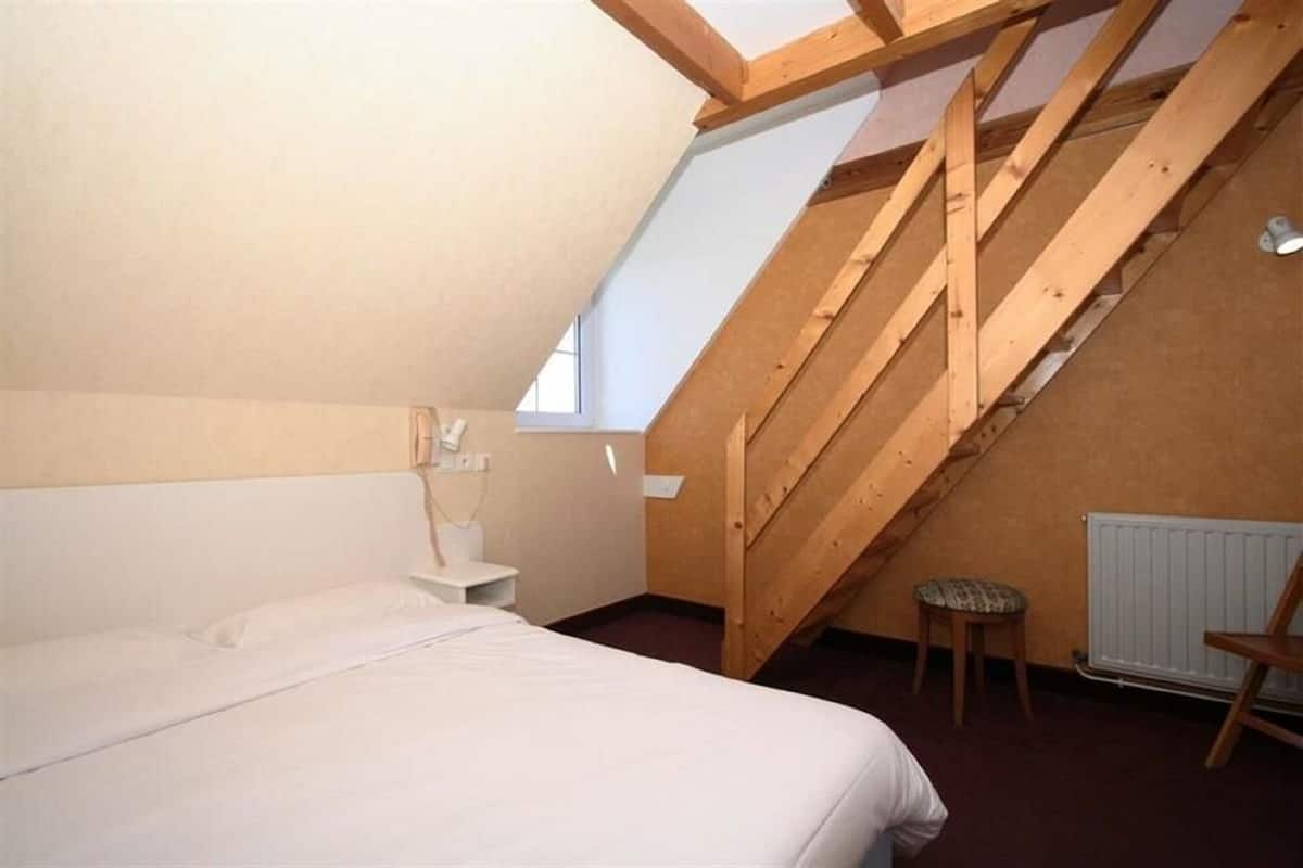 A bedroom with a sloped ceiling, a bed, a nightstand, a chair, and a radiator.