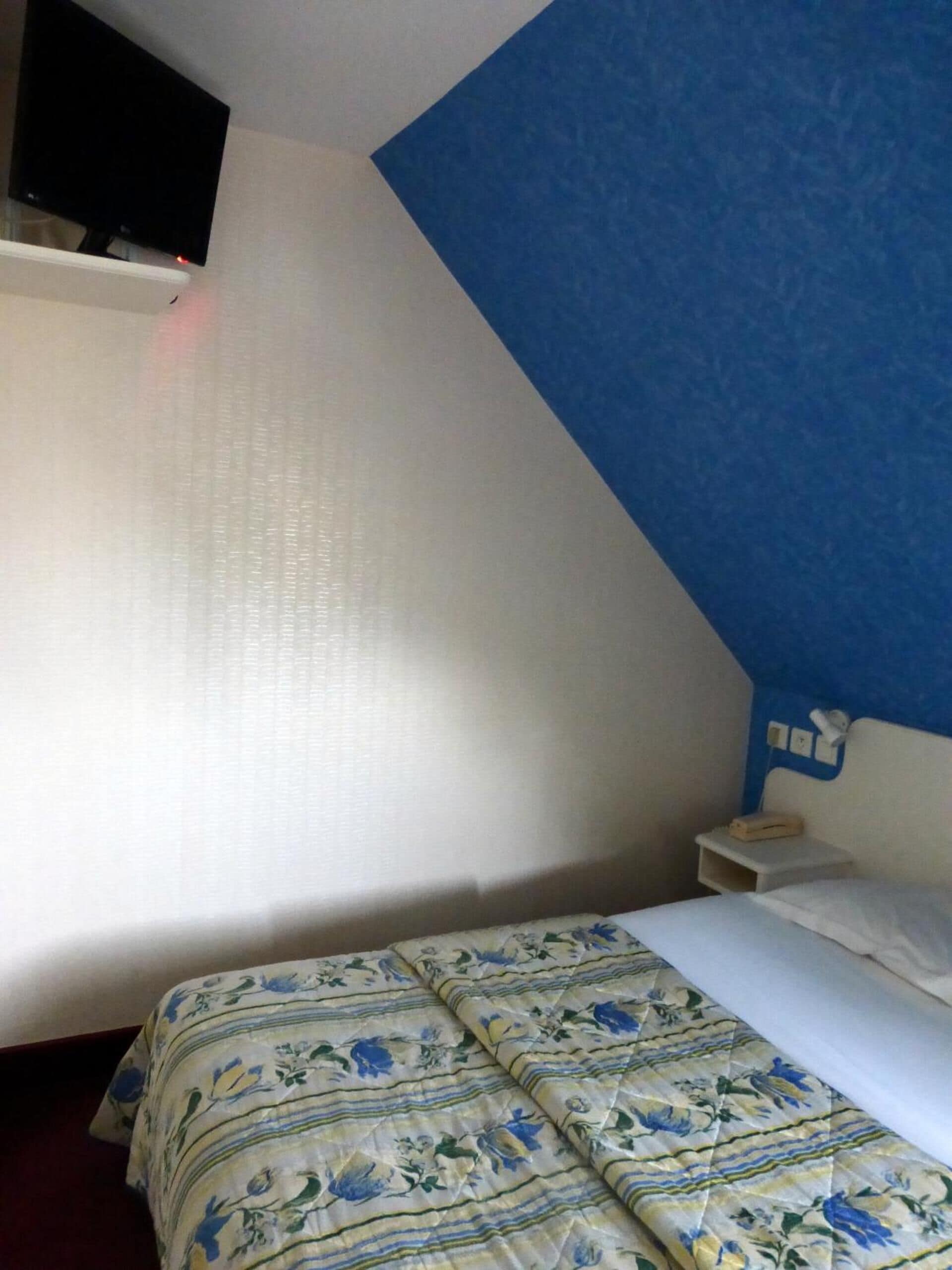 Camera da letto con un letto, un comodino, una TV a parete e una parete decorata in blu.