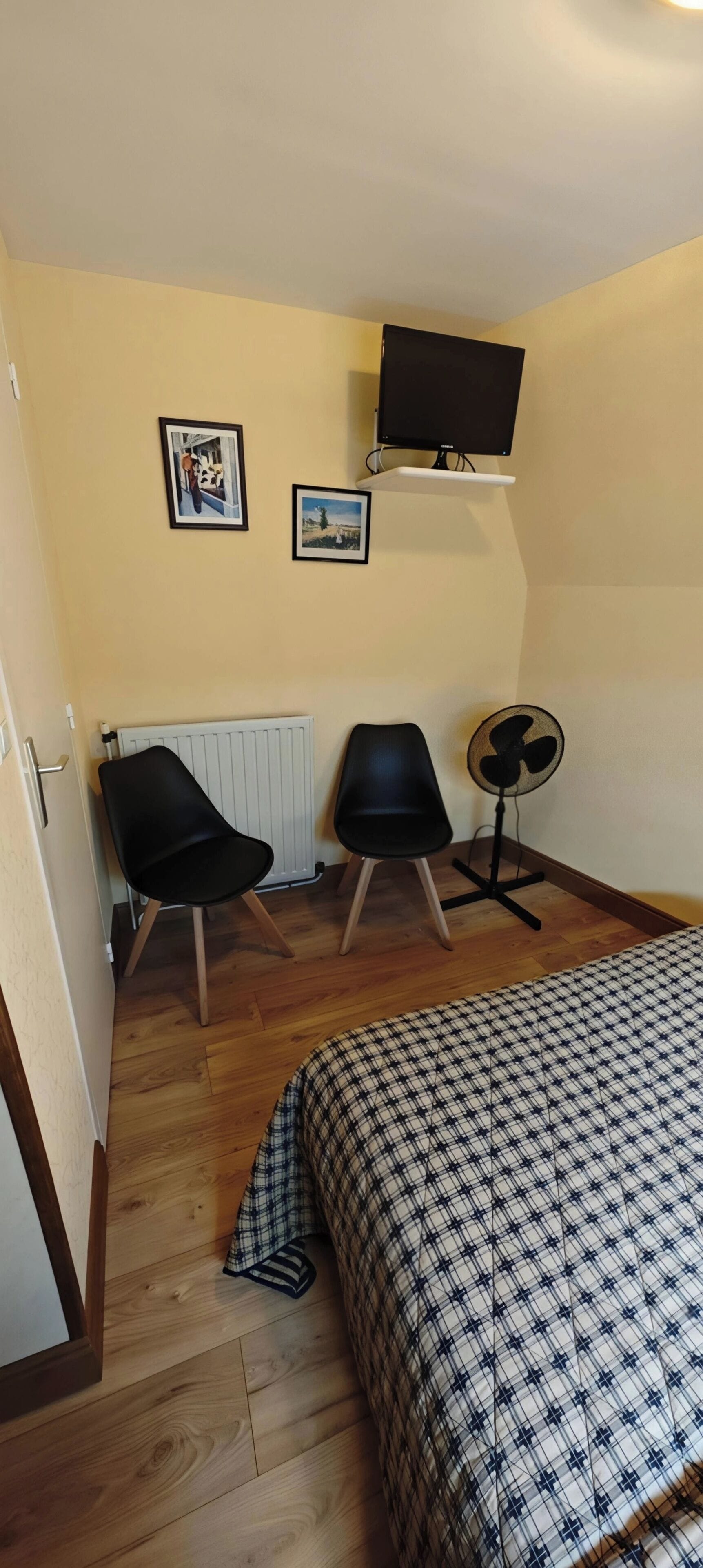 A small room with a bed, two chairs, a TV, and a fan.