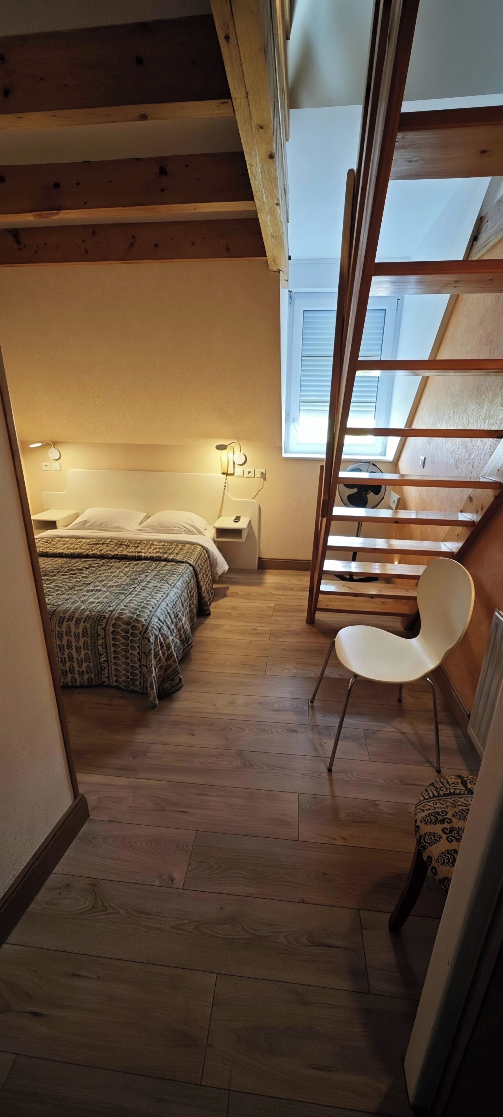 A room with a loft bed, a chair, a bedside table, and a window.