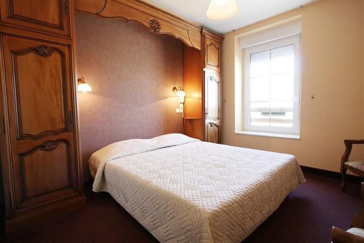 A bedroom with a large bed, wooden paneling, two wall-mounted lamps, and a window with blinds.