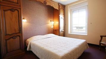 Une chambre à coucher avec un grand lit, des lambris en bois, deux lampes fixées au mur et une fenêtre avec des stores.