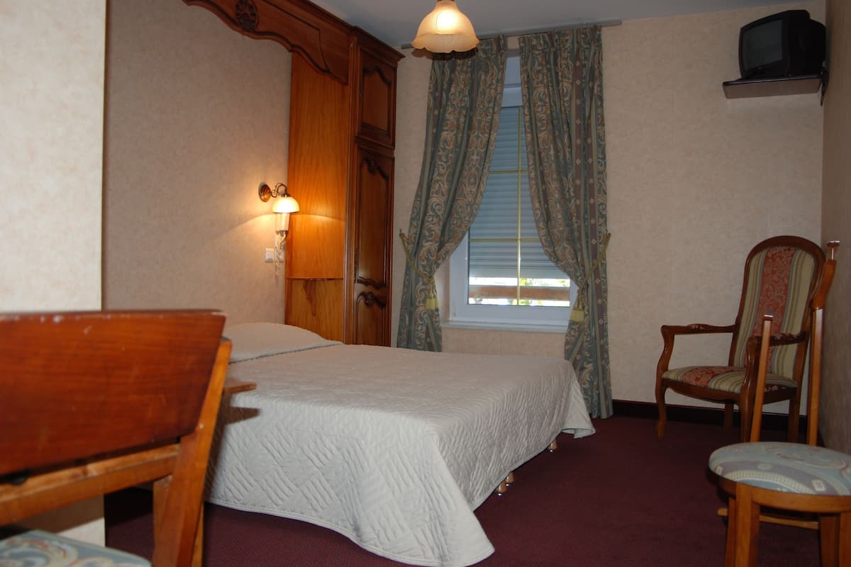A hotel room with a bed, a wooden chair, a television, and curtains.