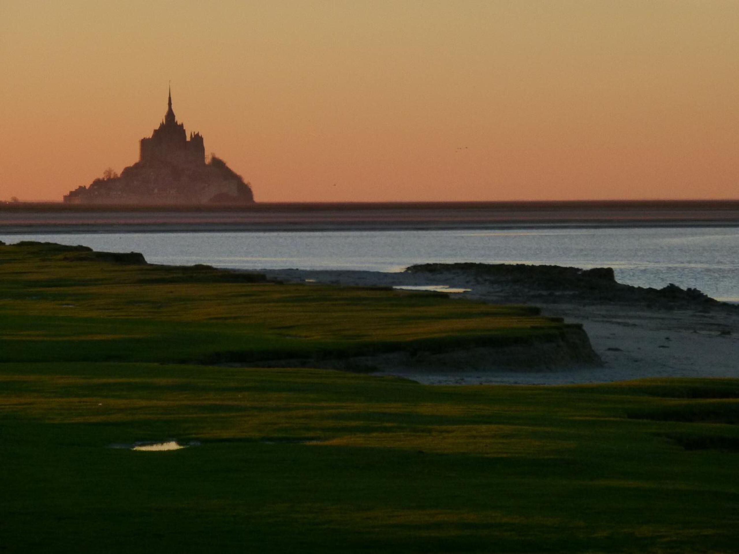 A coastal landscape with a temple-like structure silhouetted against a sunset.
