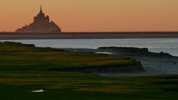 A coastal landscape with a temple-like structure silhouetted against a sunset.