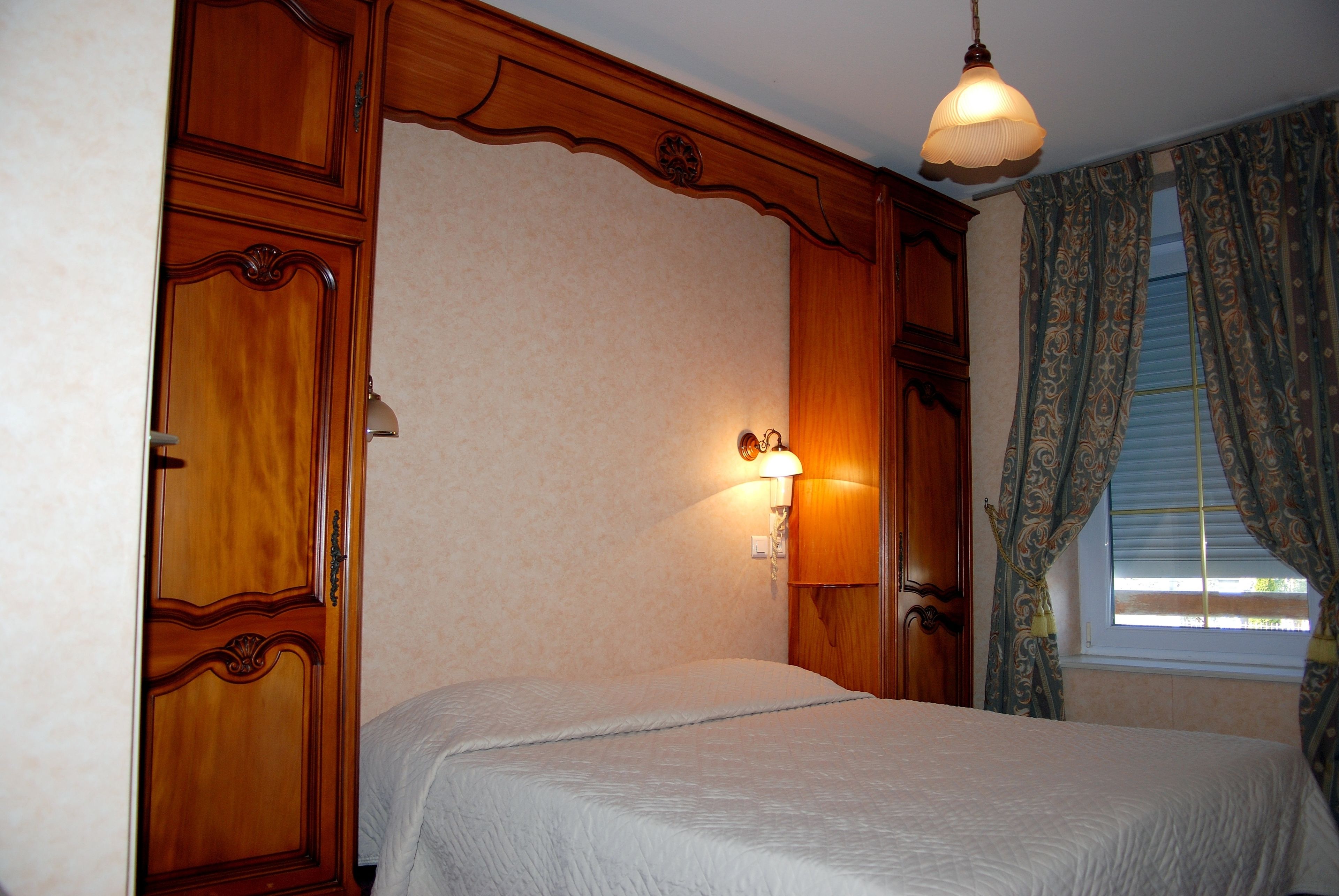 A bedroom with a bed, wooden wardrobe, and a lamp.